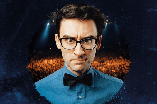 MC Hammersmith is wearing glasses, a blue shirt, and a black bow tie looks straight into the camera with a mean look on his face