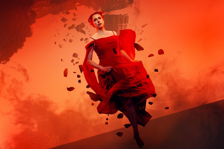 Looking fearful and frantic, a woman in a red dress runs towards the frame. The landscape behind her is red and smokey and the grand building behind her is upside down. The building falls and crumbles and she is surrounded by debris from the destruction as she runs.