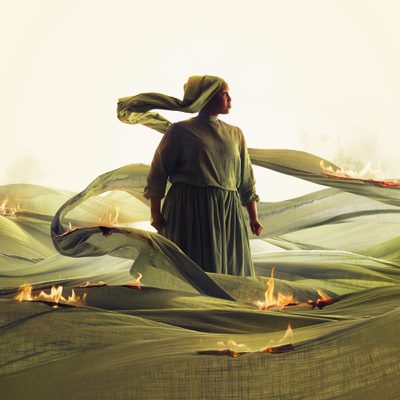 A woman in a green dress stands gracefully in a vibrant field, surrounded by tall grass and wildflowers and little fires.