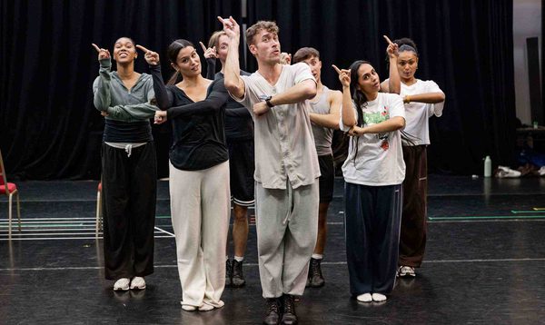 The Cinderella Ensemble are dancing together with their right hands pointing up in the air