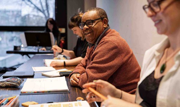 Clive Rowe, the Director is sat smiling behind a table