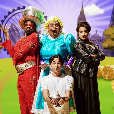 A photo of Kat B as the Genie, Clive Rowe as Widow Twankey, Fred Double as Aladdin and Natasha Lewis as Abby-na-zaaar! They are all posing together against a purple and grassy background around Aladdin, who is holding the lamp.