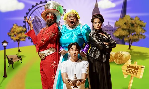 A photo of Kat B as the Genie, Clive Rowe as Widow Twankey, Fred Double as Aladdin and Natasha Lewis as Abby-na-zaaar! They are all posing together against a purple and grassy background around Aladdin, who is holding the lamp.