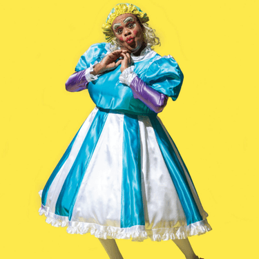 A photo of Clive Rowe dressed in a blue and white dress with a yellow wig and their hands held up to their face.