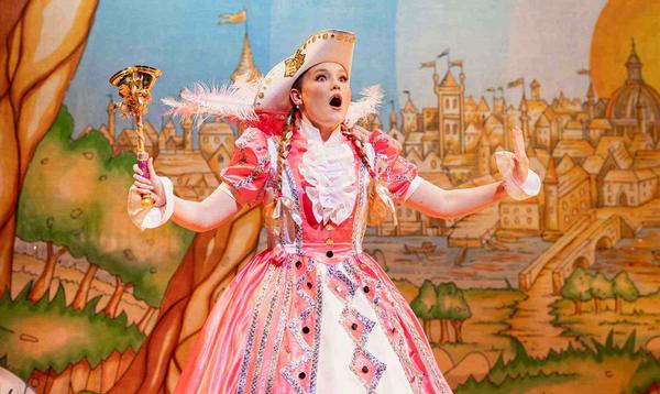 Beth Sindy as Fairy Bowbells wearing a wide pink dress, carrying a bell in her right hand and with a shocked expression on her face.