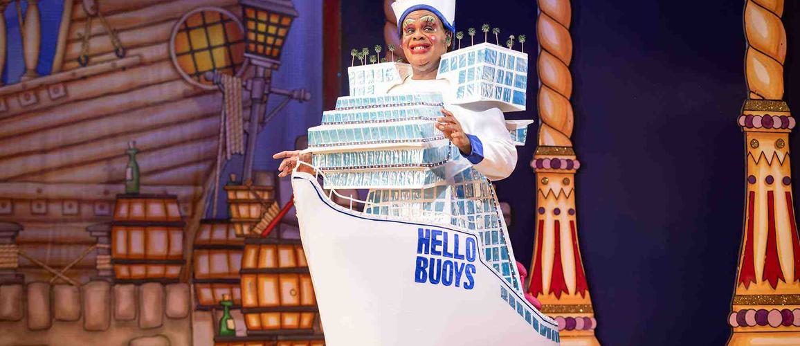 Clive Rowe as Sarah the Cook. Clive is wearing a giant dress in the shape of a ship, that says HELLO BUOYS on the side of it.