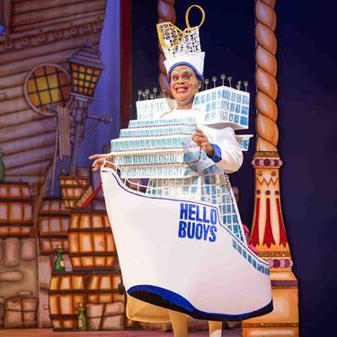 Clive Rowe as Sarah the Cook. Clive is wearing a giant dress in the shape of a ship, that says HELLO BUOYS on the side of it.