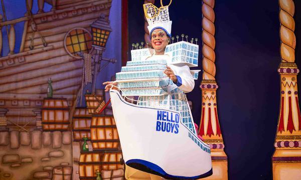 Clive Rowe as Sarah the Cook. Clive is wearing a giant dress in the shape of a ship, that says HELLO BUOYS on the side of it.