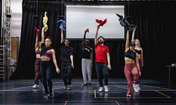 The Dick Whittington and his Cat Ensemble are mid dance with their right hands up in the air holding a piece of material/clothing.