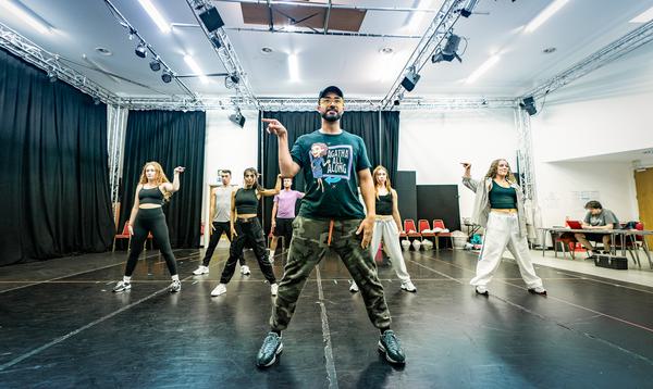 A photo of Myles Brown, the choreographer, and the Aladdin Ensemble. They are dancing, stood with legs outstretched and their right hands pointing out to the right.