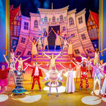 Full Company pose on stage in front of Hack-ne-lah Town Hall in the finale of Aladdin.