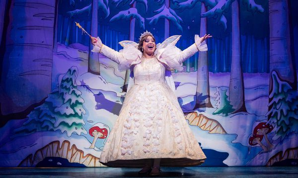 Jade Johnson as the Fairy Godmother has arms and her wand outstretched with a beaming smile on her face.