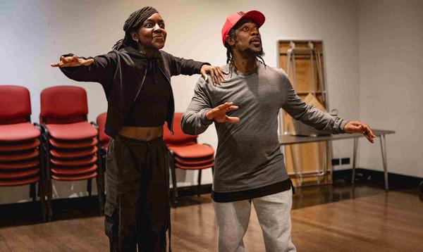 Kandaka Moore as Dick Whittington is holding onto one shoulder of Kat B as Tommy the Cat and they're both looking out front with excited expressions.