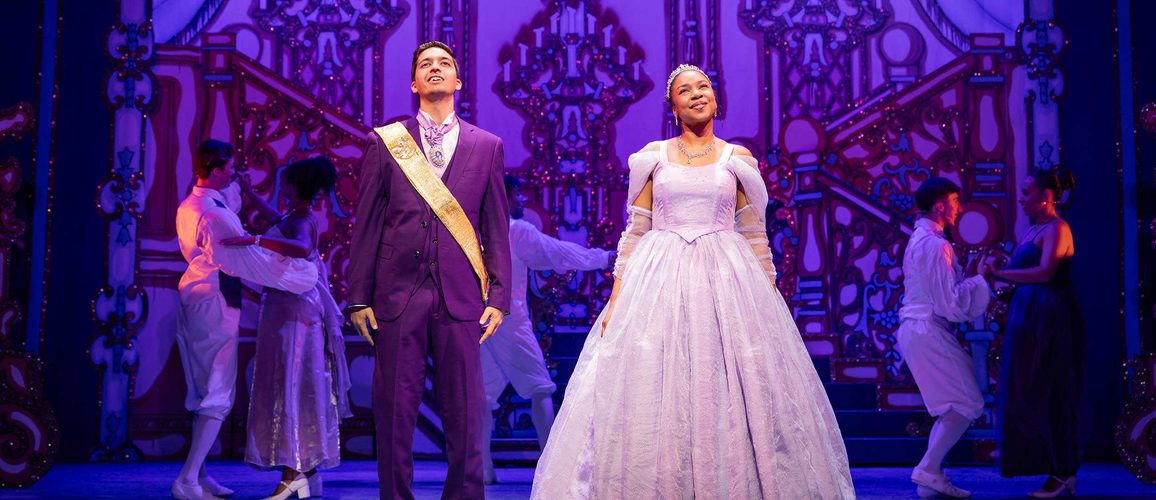 Luke Latchman as Prince Charming and Siobhan James as Cinderella stand side by side at the Ball with loving expressions on their faces.