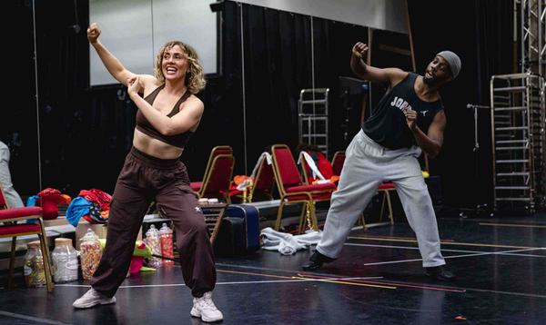 Nicole Reeves and Wilson Kiiru are leaning into the space with one leg and poking their heads in with grins on their faces.