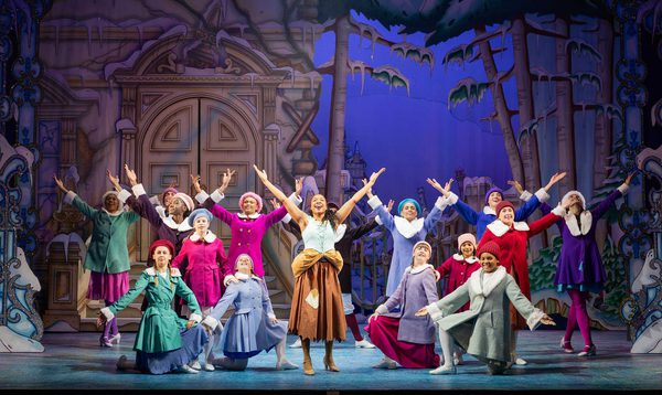 Siobhan James as Cinderella and the Full Ensemble pose together on stage with their arms up in a v position.