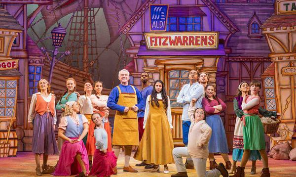 Tony Timberlake as Alderman Fitzwarren and Aryana Ramkhalawon as Alice Fitzwarren as posing in the centre of the space with the Dick Whittington and his Cat Ensemble and Young Ensremble posing around them smiling.