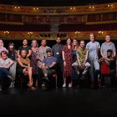 A photo of the Hackney Empire Team stood and sat on the main stage, all posing towards the camera with the auditorium behind them.