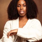Jasmyn Fisher-Ryner wearing a white cardigan and sat sideways on a chair staring straight at the camera