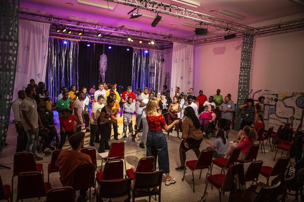 A group of young people all wearing colourful t-shirts are dancing together in the rehearsal space.