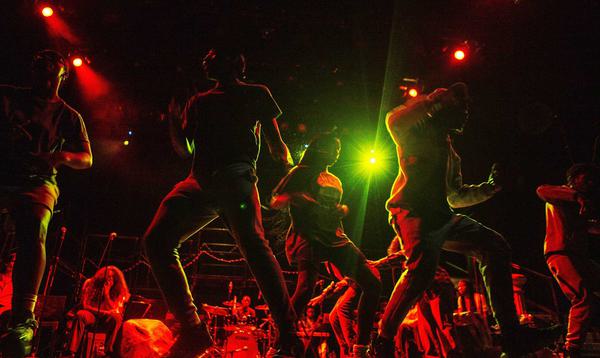 The Company of ADP 2021 dancing at the front of the stage with red and green stage lights on them.