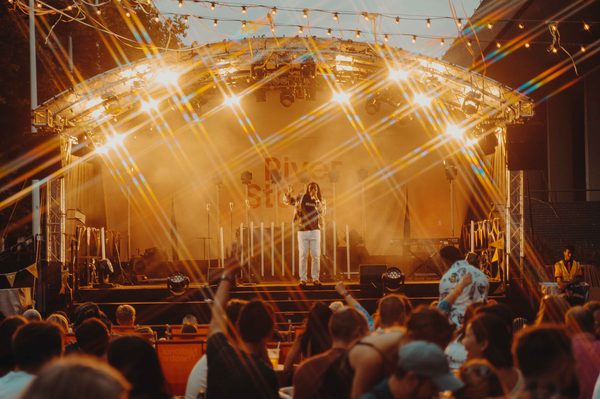 A photo taken from the back of the crowd at River Stage 2022 on the Southbank showing one performer on stage surrounded by bright stage lights.