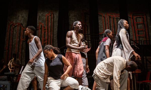 One lone figure stands in the centre of a circle of people as they face away from him, in the centre of Hackney Empire's stage