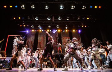 A group of young dancers on Hackney Empire's stage with one arm flung in the air as they move side to side.