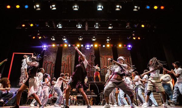 A group of young dancers on Hackney Empire's stage with one arm flung in the air as they move side to side.