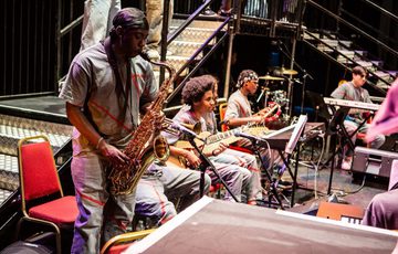 A group of young musicians playing the saxophone, guitar and keyboard on Hackney Empire's stage