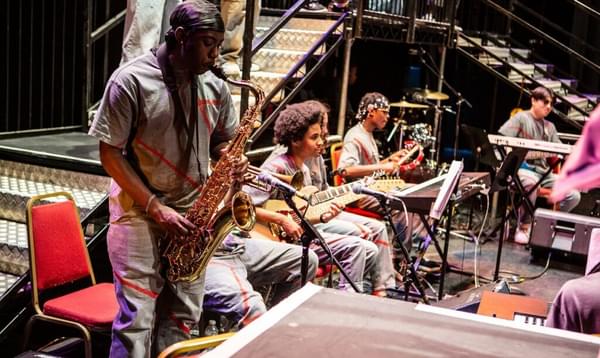 A group of young musicians playing the saxophone, guitar and keyboard on Hackney Empire's stage