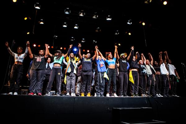 A group of young people bowing at the end of Only Joy Aloud 2022. They are all holding hands with arms in the air about to bow.