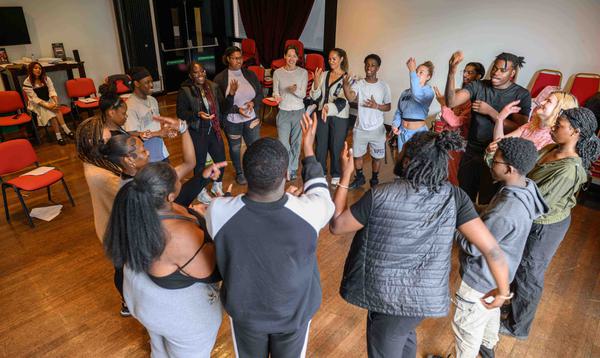 A group of young people are dancing together in a circle in the middle of the rehearsal space with Leona Lewis