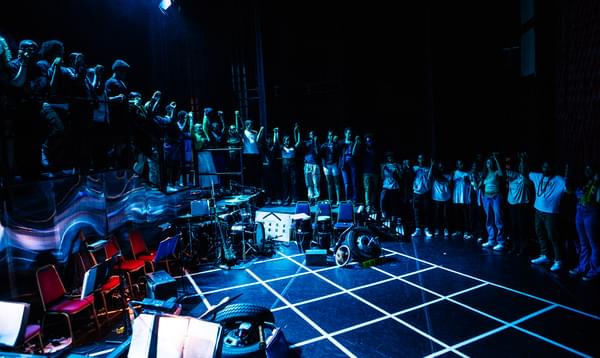 A photo on stage at Hackney Empire showing the whole Company of the Artist Development Programme 2023 in a circle around the stage all holding hands.