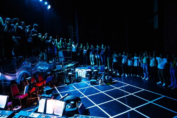 A photo on stage at Hackney Empire showing the whole Company of the Artist Development Programme 2023 in a circle around the stage all holding hands.