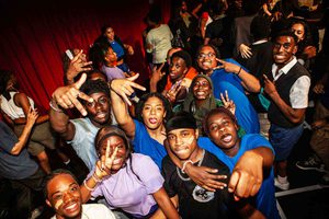 A photo taken backstage showing a group of young people all in colourful clothing posing towards the camera and smiling