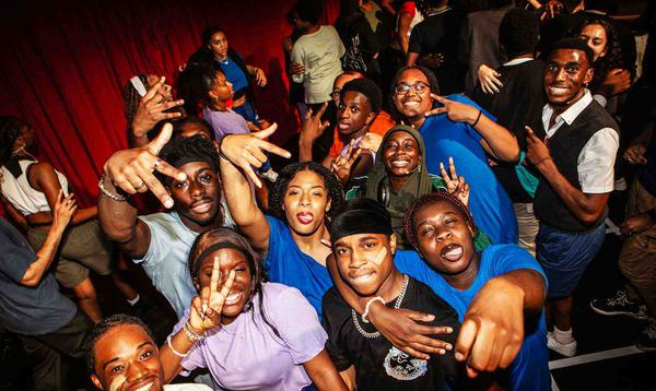 A photo taken backstage showing a group of young people all in colourful clothing posing towards the camera and smiling