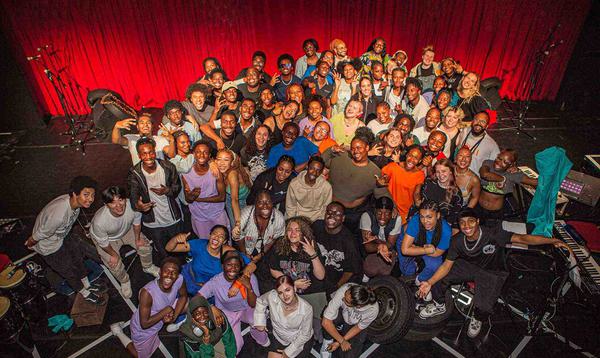 A group shot of the whole Company and Creative Team showing about 70 people posing together on our stage with the red curtain behind.