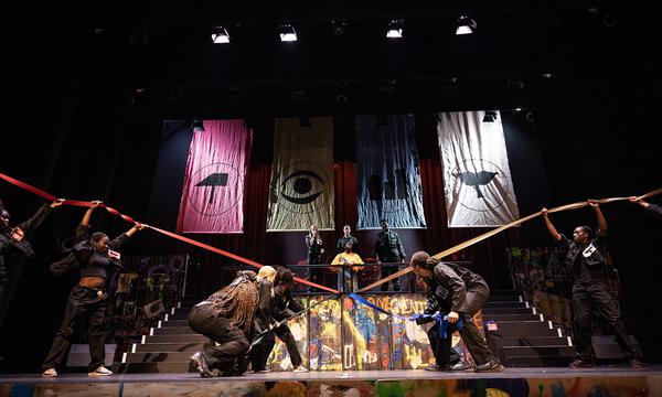 The ADP 2024 Company performing on stage, with several cast members pulling long bits of thick ribbon in different directions on the stage.