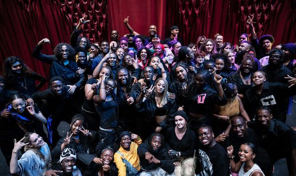 A full group shot of all of the participants and people involved in ADP 2024 taken on the Hackney Empire stage with the red curtain behind.