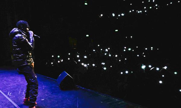 A photo of musician Prinz performing on stage with the lights from phone lighting up the auditorium.