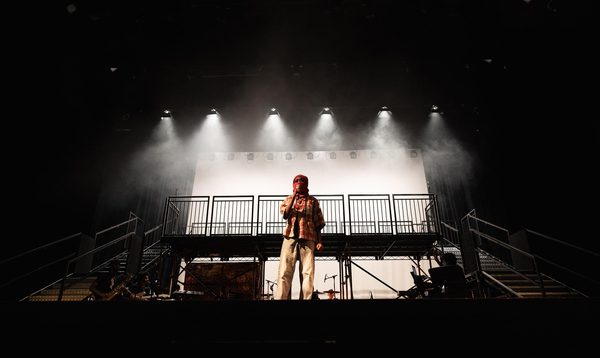 The character Joy from The Kindling is stood in the centre of the stage speaking into the microphone