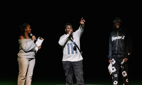 The hosts and participator of Alter Ego is standing on stage and the participant is talking into the microphone with his left hand in the air as though he saluting the audiences