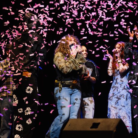 The winner of Alter Ego standing on stage with a shocked expression on their face while pink confetti continues to fall on them.