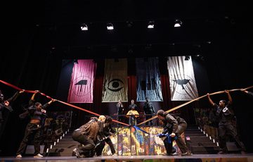 The ADP 2024 Company performing on stage with large sections of ribbon billowing out in different colours from the central figure on stage.