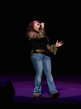 A young person is performing on the ,main stage holding the mic close to their mouth as they sign into the microphone.