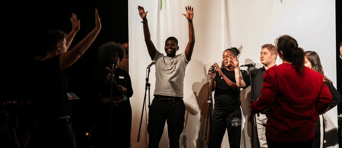 A group of young people with their hands up in the air are participating in The Studio and