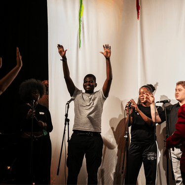 A group of young people with their hands up in the air are participating in The Studio and