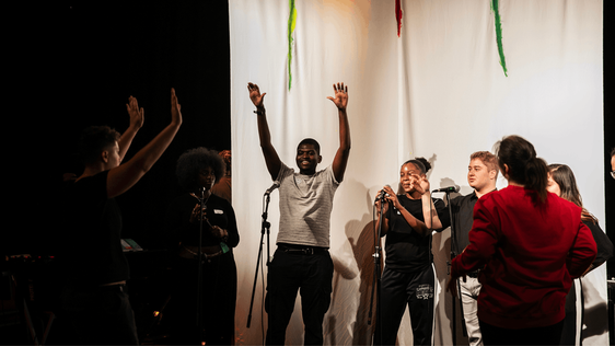 A group of young people with their hands up in the air are participating in The Studio and