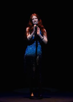 A young person wearing a deep blue dress.is singing on the ,main stage holding the mic close to their mouth as they sign into the microphone.